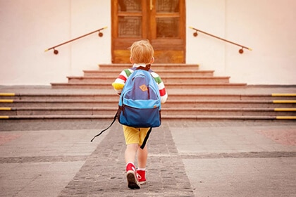 a child wearing a backpack heading into a school building