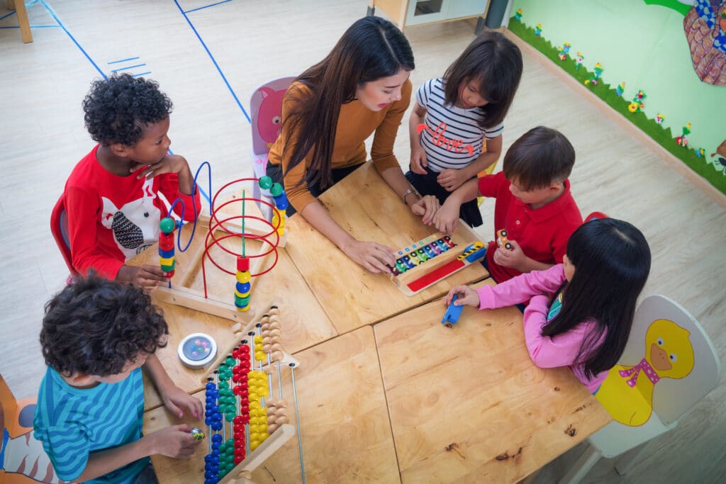 several children play with simple toys as a teacher watches over