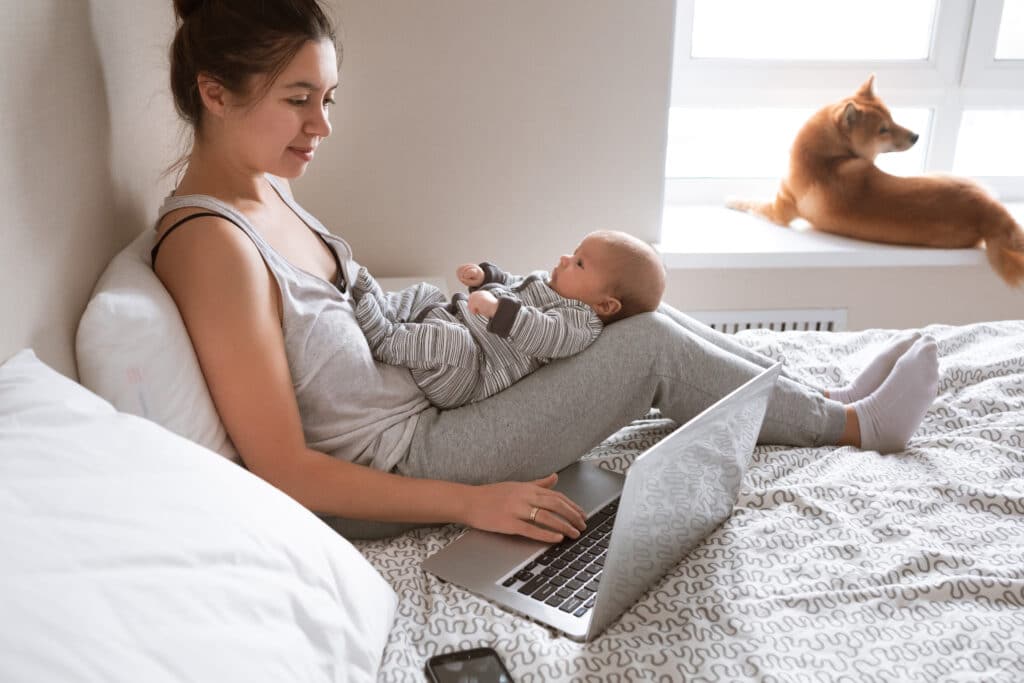 woman with a baby in her lap works on her computer with one hand