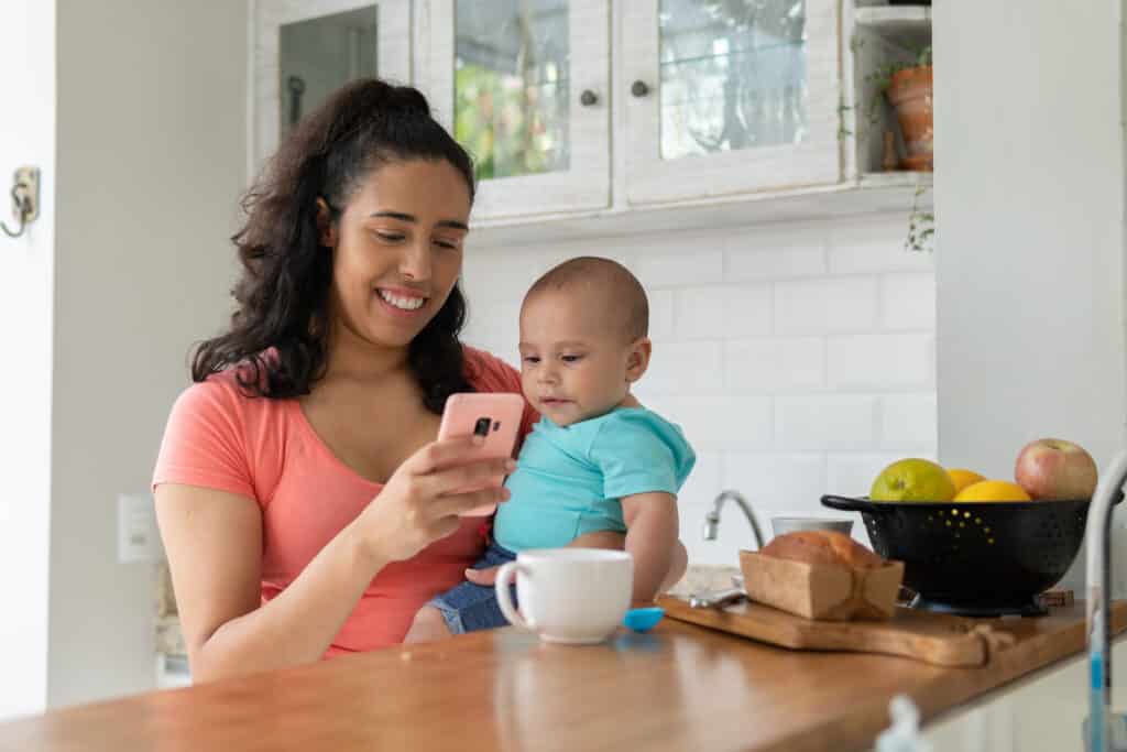 a mother looks at her phone while holding an infant