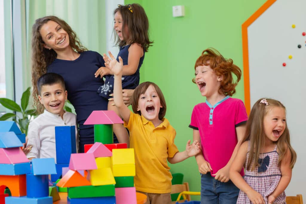 a preschool teacher and five students pose triumphantly in front of a castle made out of blocks. If you're hosting a preschool open house, activity centers like blocks can help keep children busy.