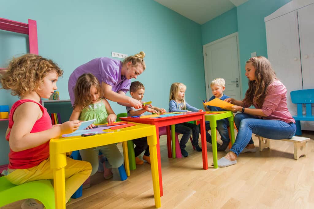 two daycare staff members help five students with an arts and crafts project