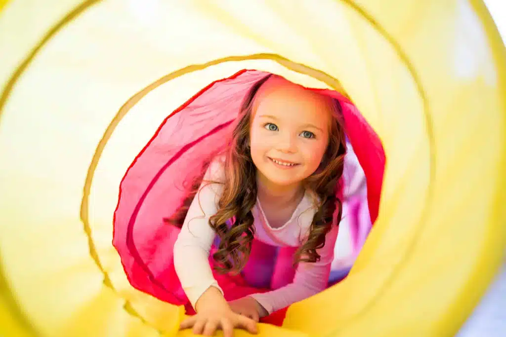 a toddler crawl through a red and yellow play tunnel