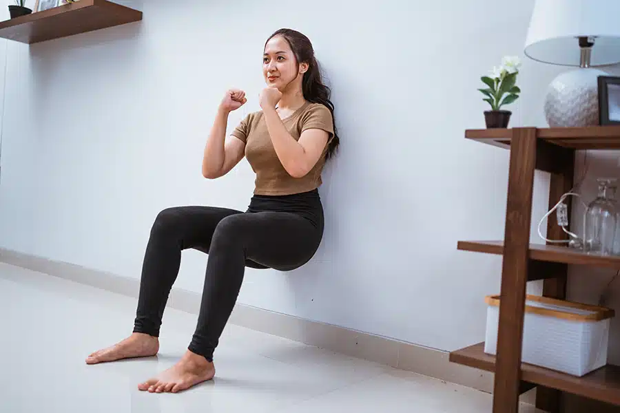 a woman in black pants and brown shirt doing a wall squat