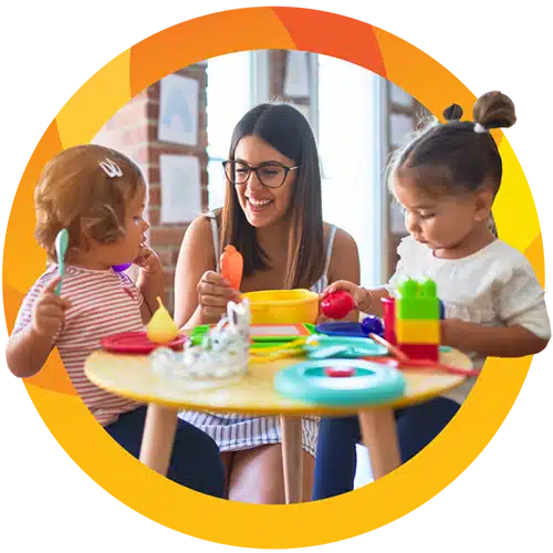 a teacher helps two toddlers play with blocks and play food at a small table