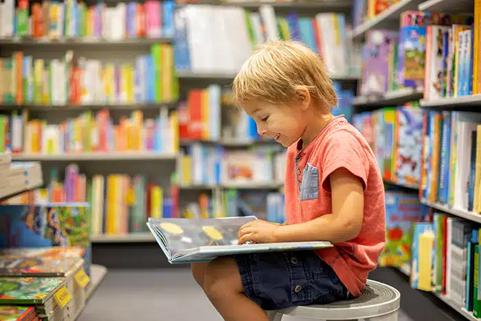 A preschool-age boy reads a book in the library.