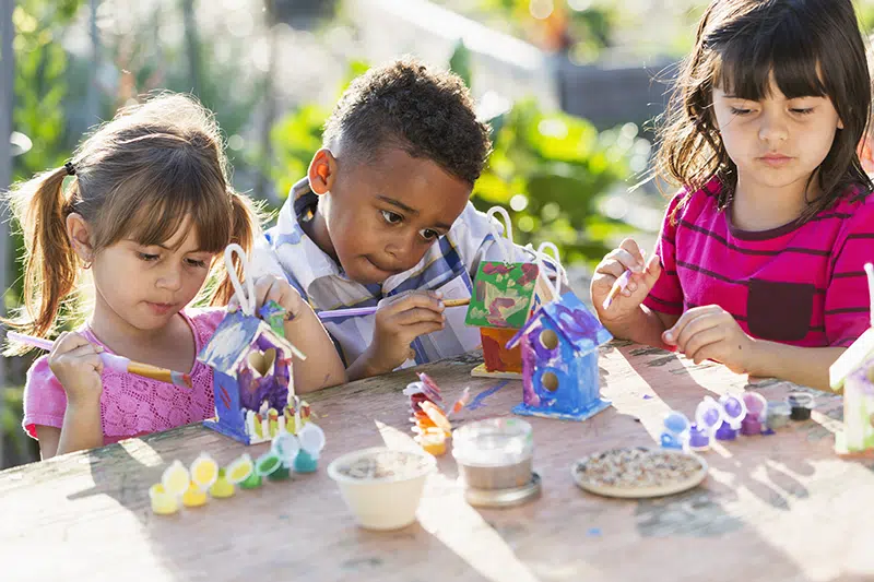 three children participating in associative play by painting birdhouses