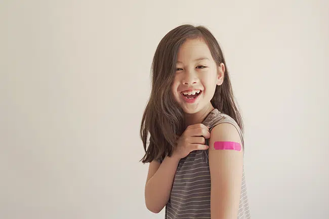 A young girl smiles at the camera while showing off a pink bandage on her arm