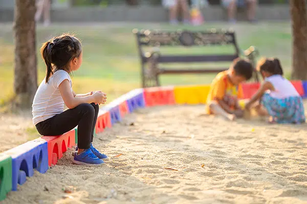 Child takes part in onlooker play in big sandbox.