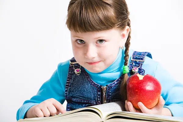 Young girl eats an apple and looks at a book while at daycare