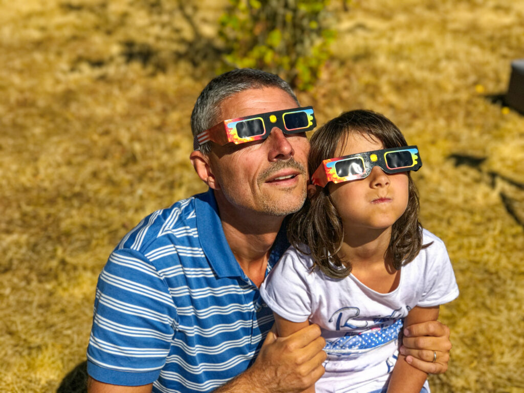 Adult and child view solar eclipse together using correct glasses.