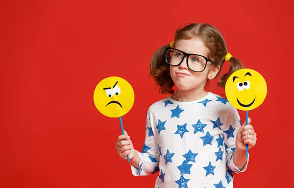 preschooler holds up a frowny face and a happy face to learn about emotions