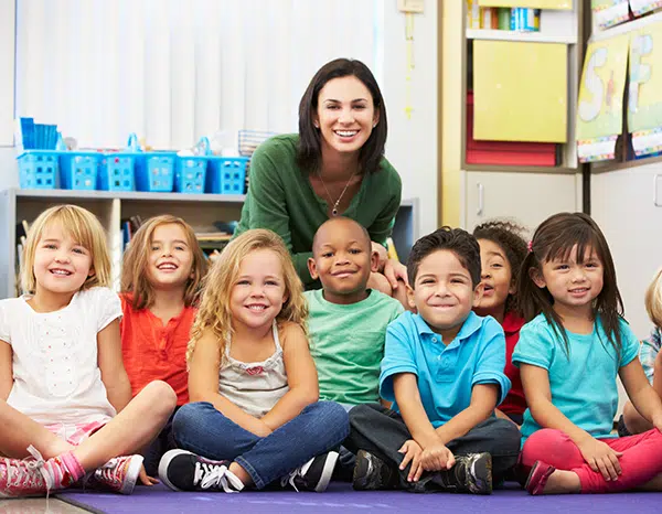 teacher smiles in front a group of sitting chldren