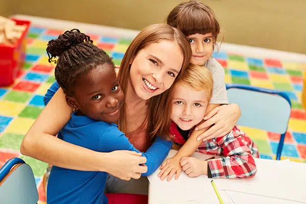 a preschool teacher is hugged by three of her students