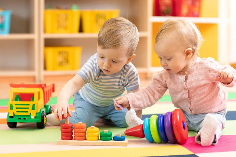 a couple of infants in a classroom setting. they are playing with stackable rings.