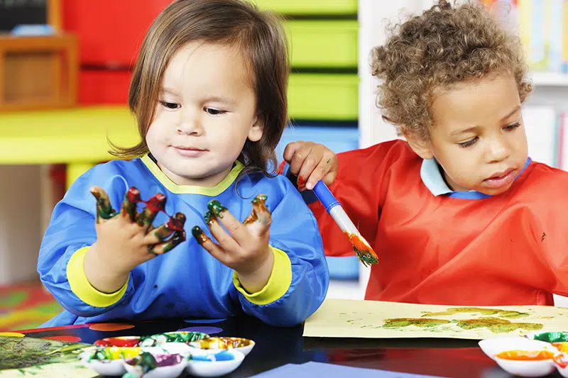 a bemused young child looks at their paint covered hands
