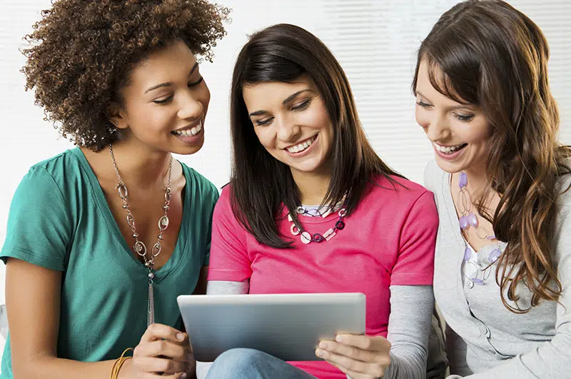 Three teachers all looking at a tablet held by the middle one