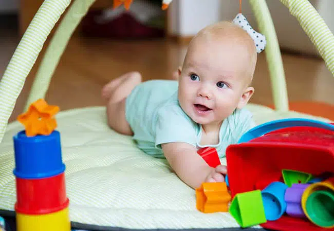 a baby on their tummy beneath a handing mobile