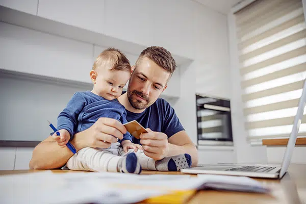 a dad with his toddler seated on top of a table, both looking at a credit card
